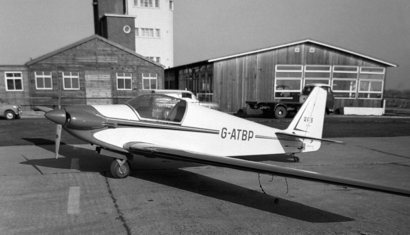 G-ATBP on the apron, black and white, older hangars and a control tower behind