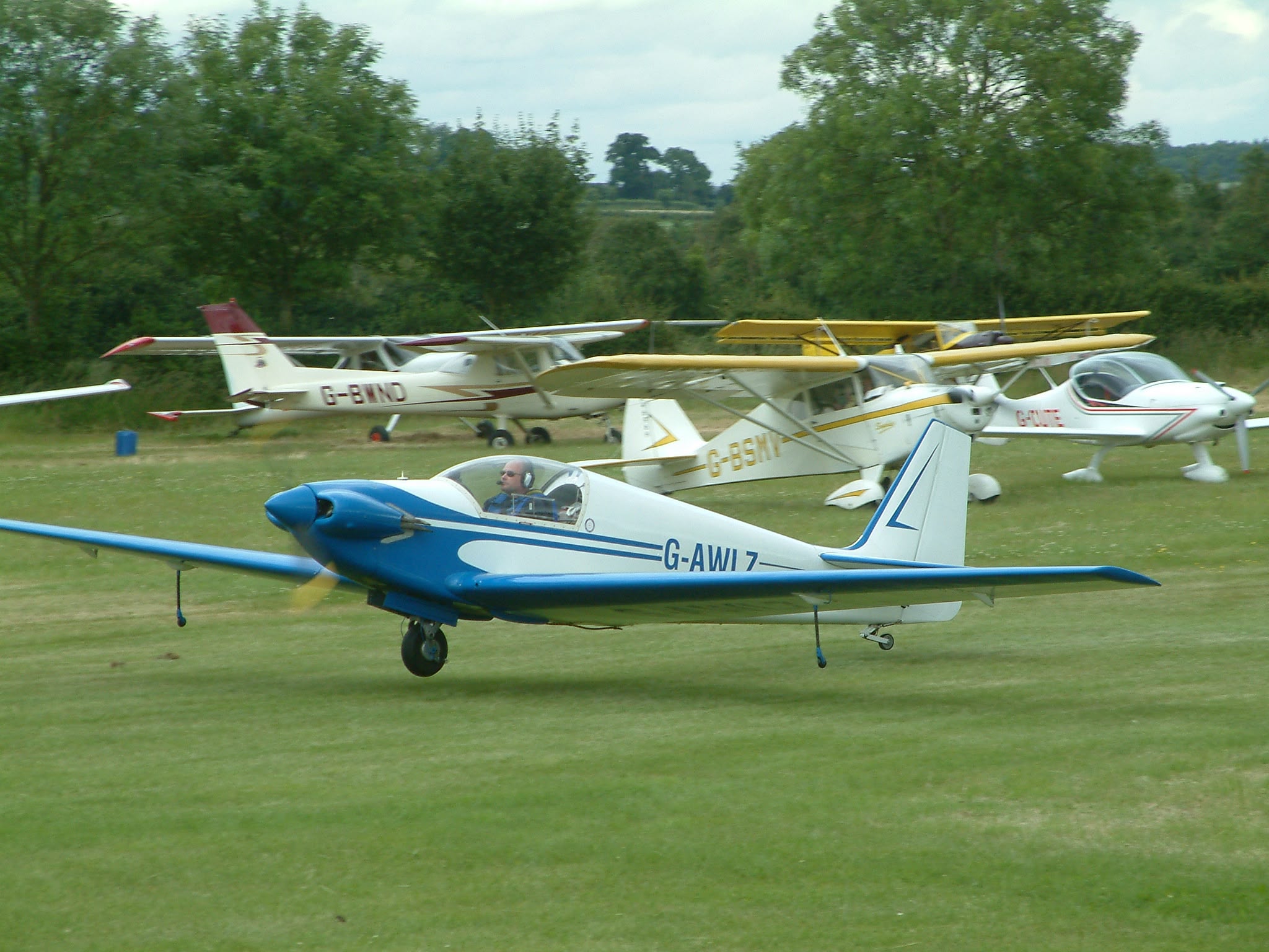 G-AWLZ landing at a fly-in, other aircraft parked behind