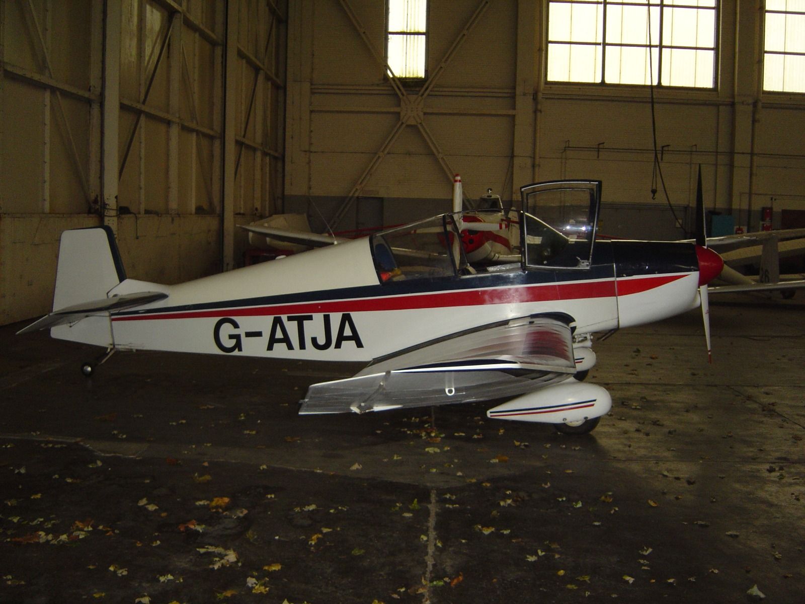 A vintage Jodel light aircraft parked inside a large historic hangar