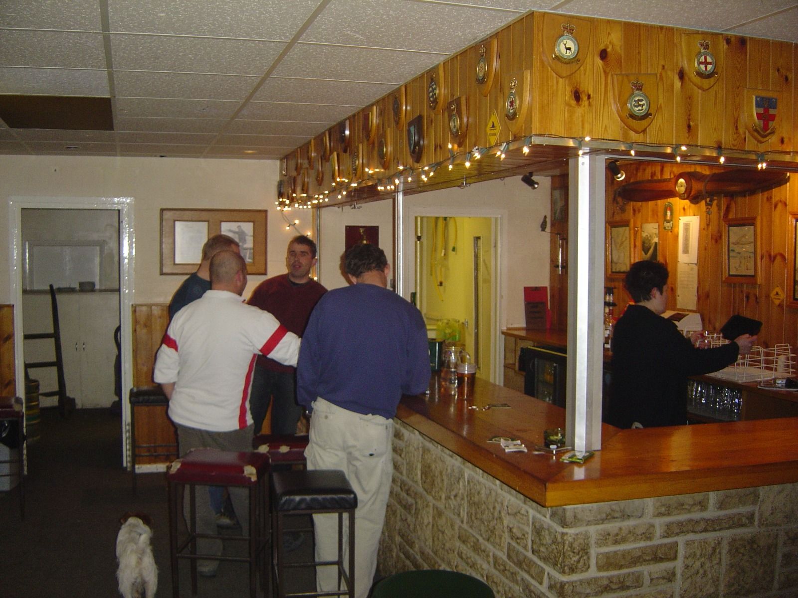 A group of people at a wood-panelled club bar decorated with squadron plaques and fairy lights