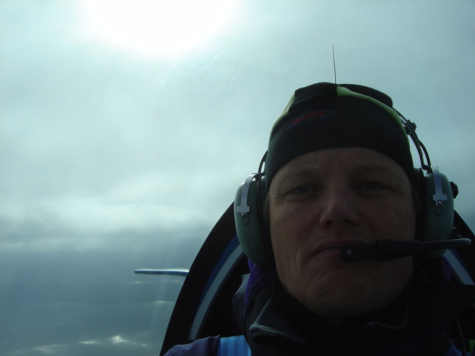 A pilot wearing a headset and beanie, backlit by a bright sun through the cockpit canopy