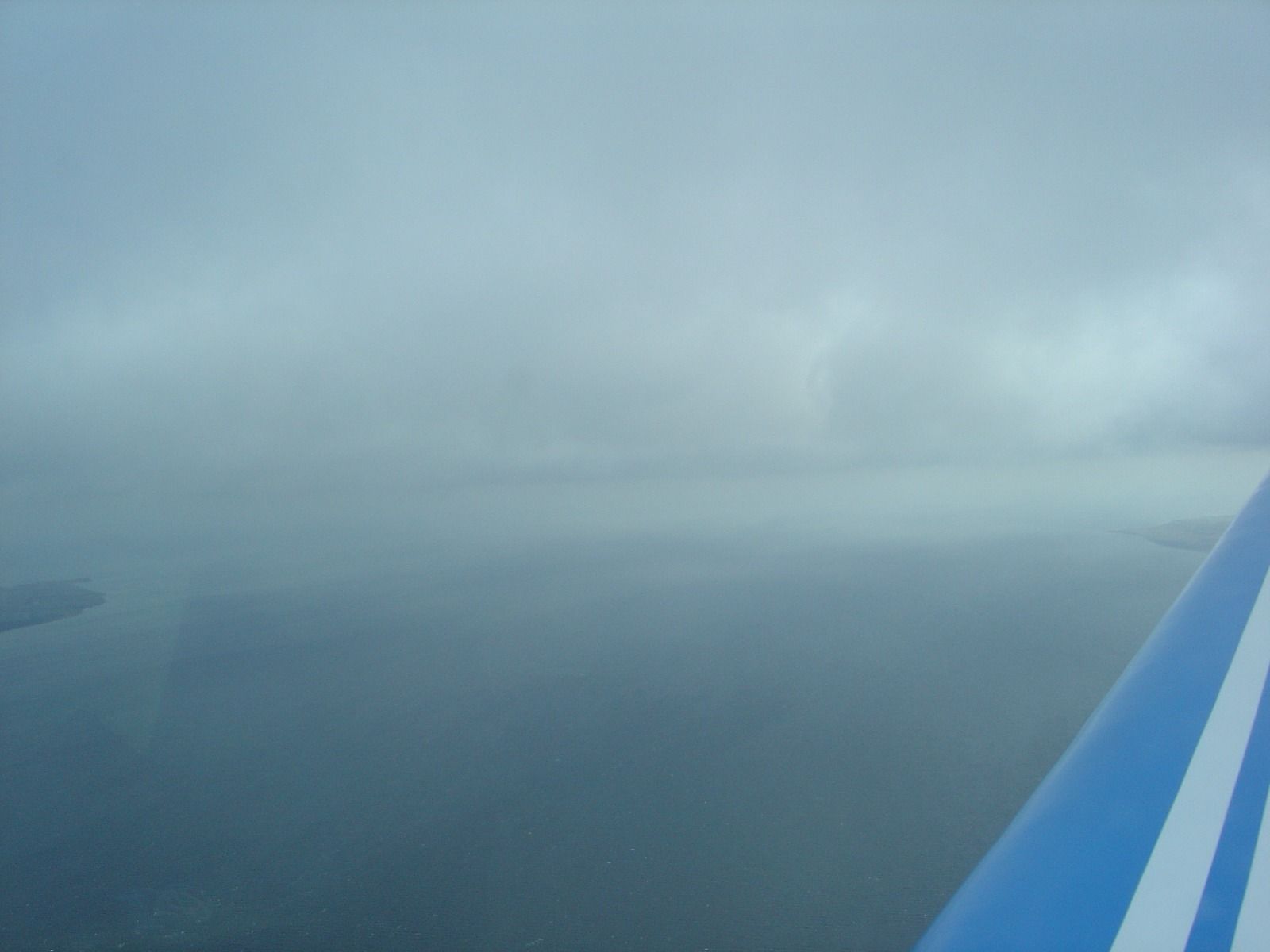 A hazy, near-featureless view over water from a cockpit, with the striped wing of the aircraft visible at the edge