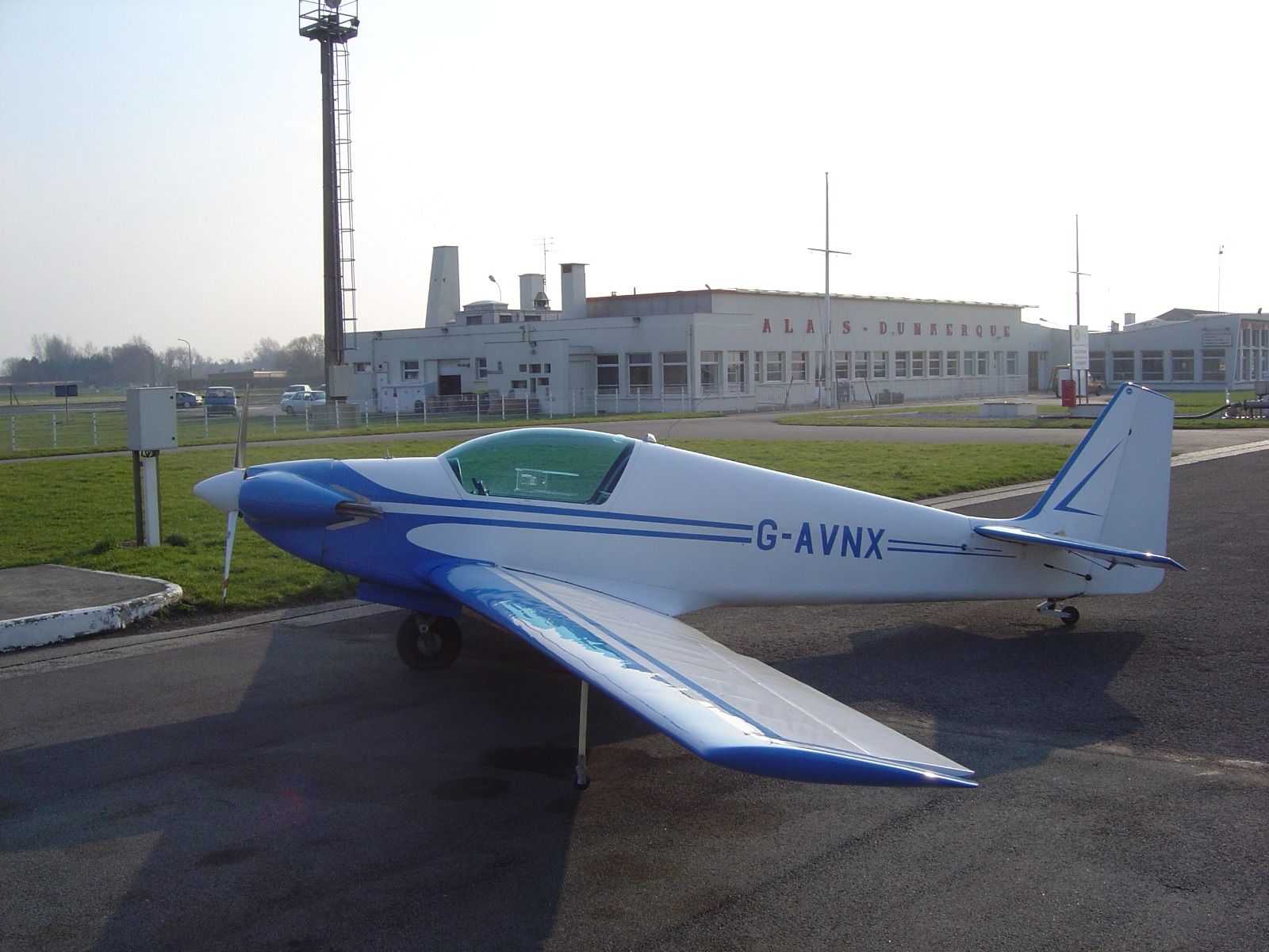 G-AVNX parked on the apron at Calais airport in front of a low white building lettered ALAIS-DUNKERQUE, with a fuel hose visible at the tail