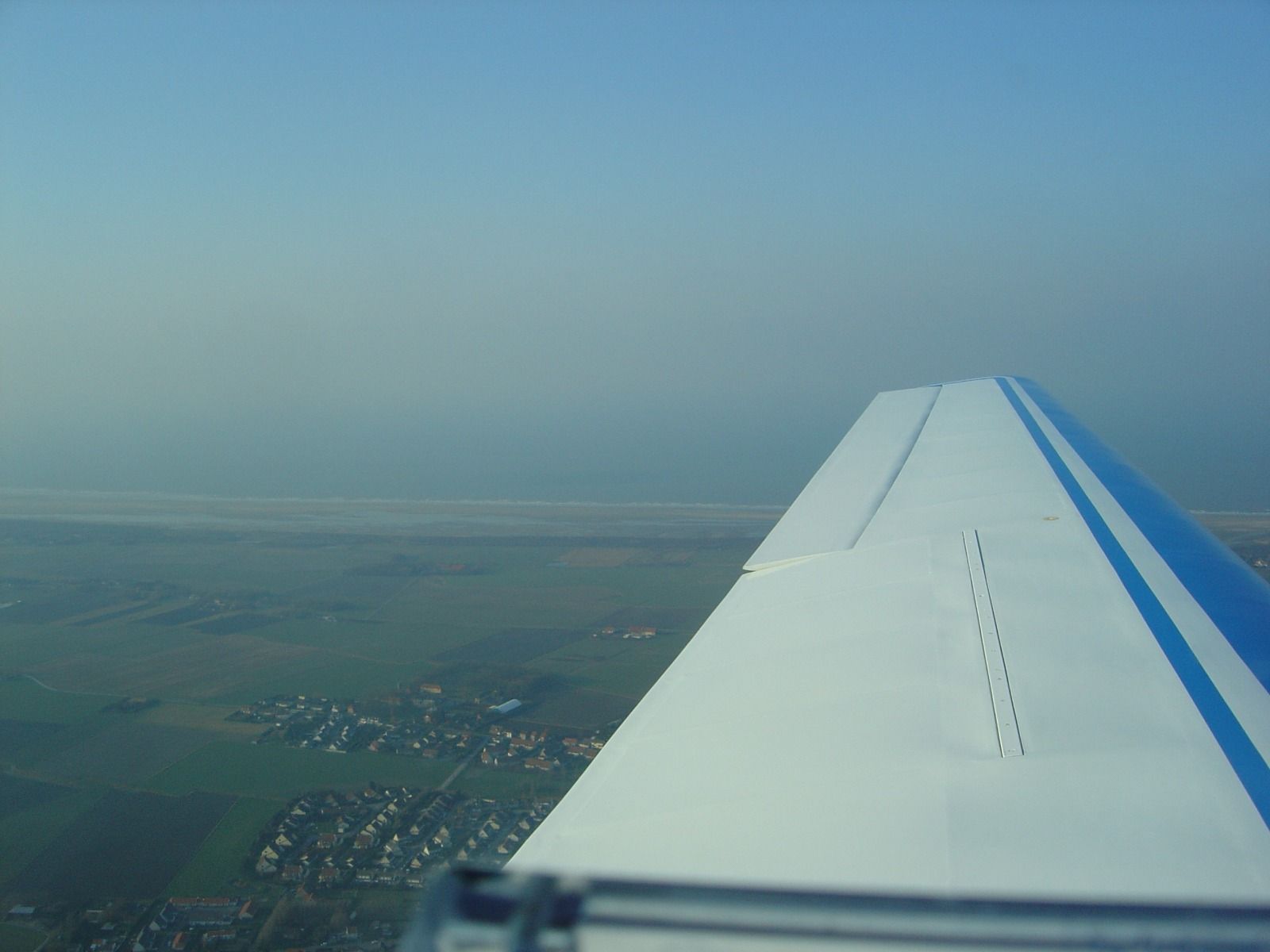 A wing view over a hazy seaside town with a sandy beach and dune line, seen under overcast light