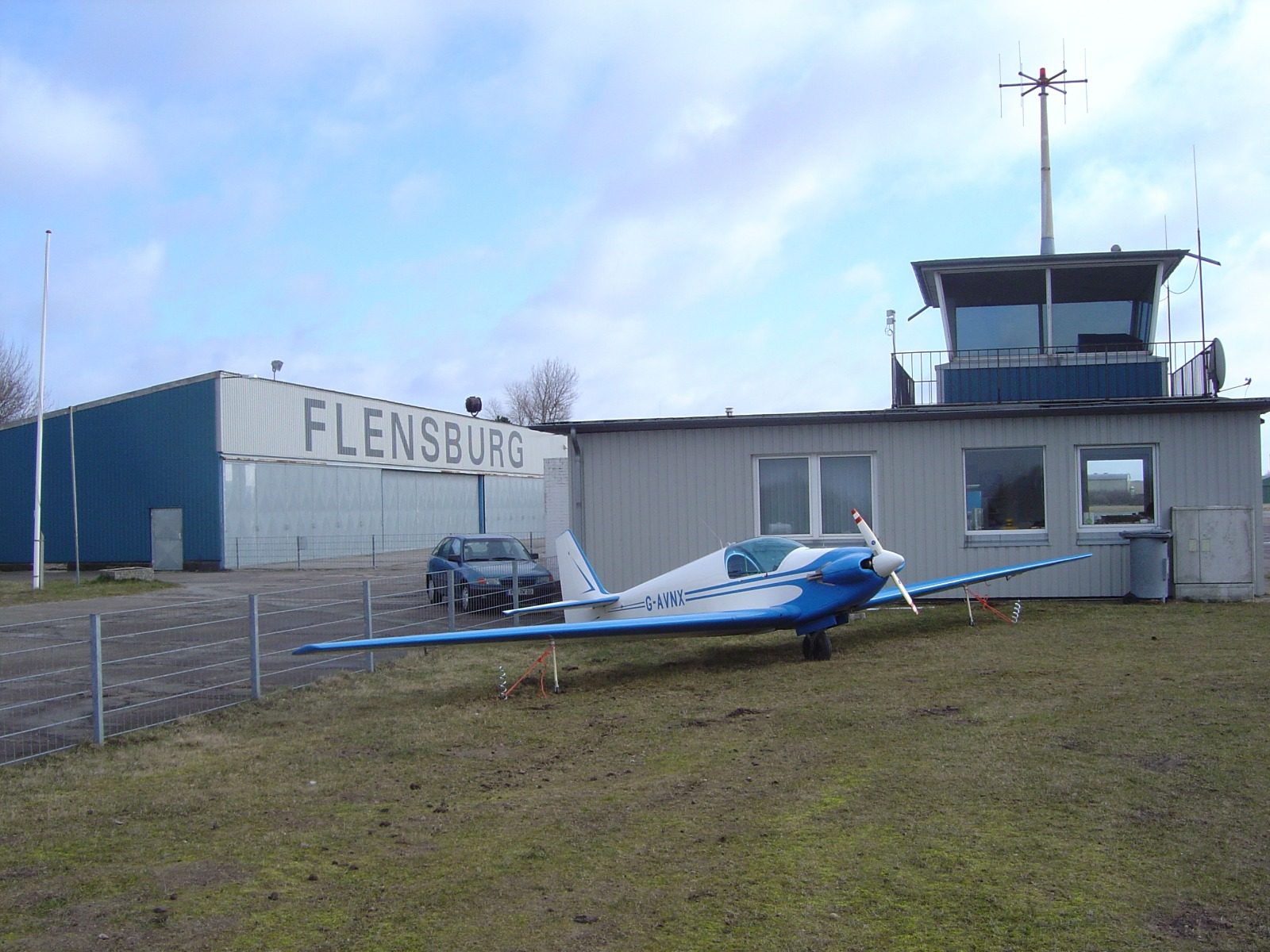 G-AVNX tied down on the grass at Flensburg, the terminal and control tower behind
