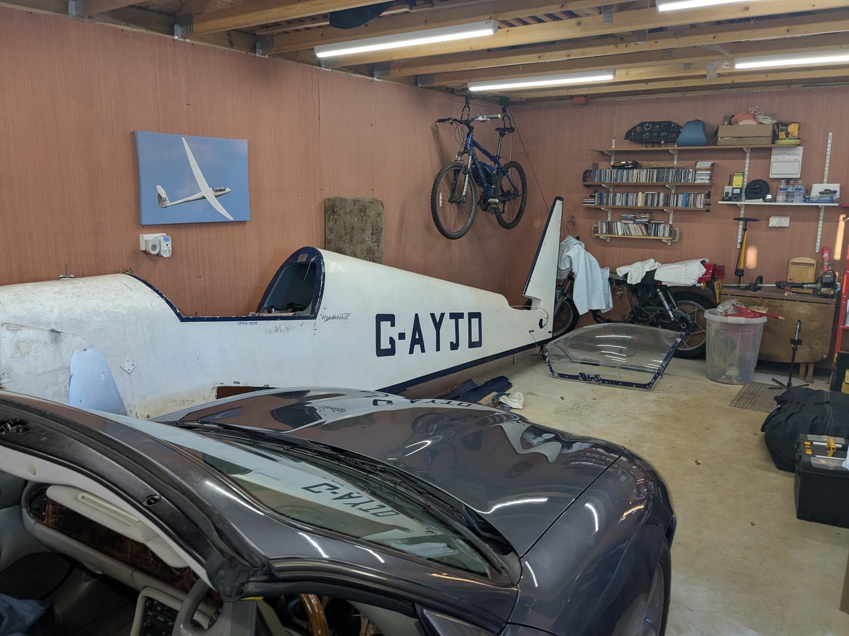 G-AYJD’s fuselage stored in a home garage during the rebuild, registration also visible on a car parked in front