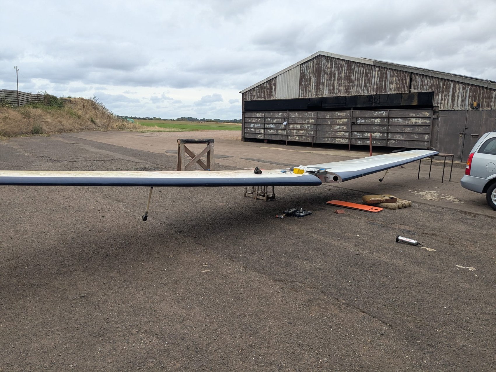 G-AYJD wing laid out on the ground at an airfield, hangar behind