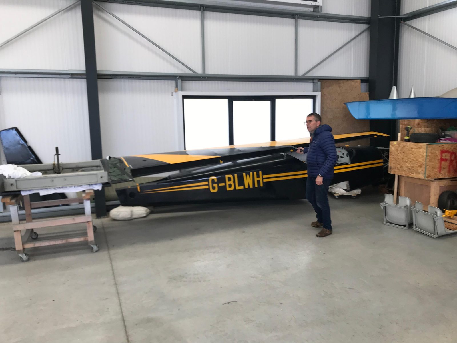 G-BLWH fuselage on a workbench in a hangar, an owner standing alongside