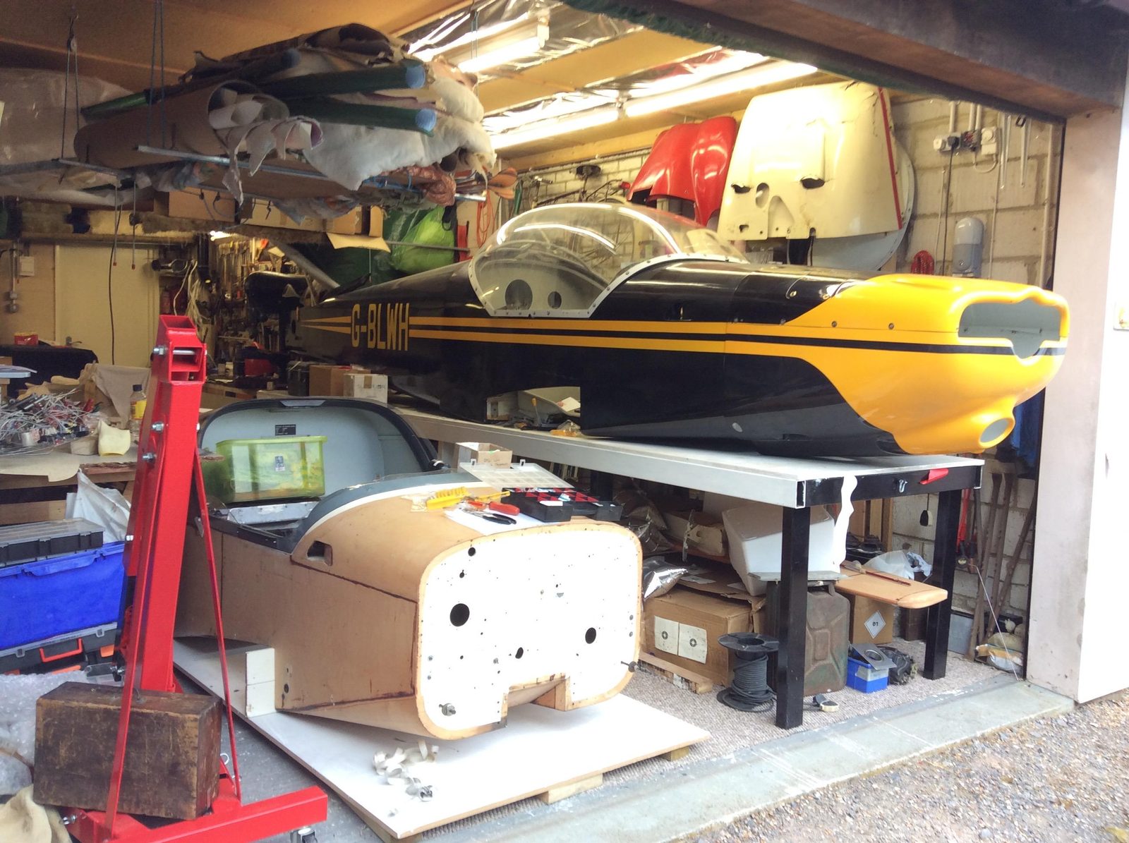 G-BLWH fuselage in the black and yellow scheme, inside a crowded garage workshop
