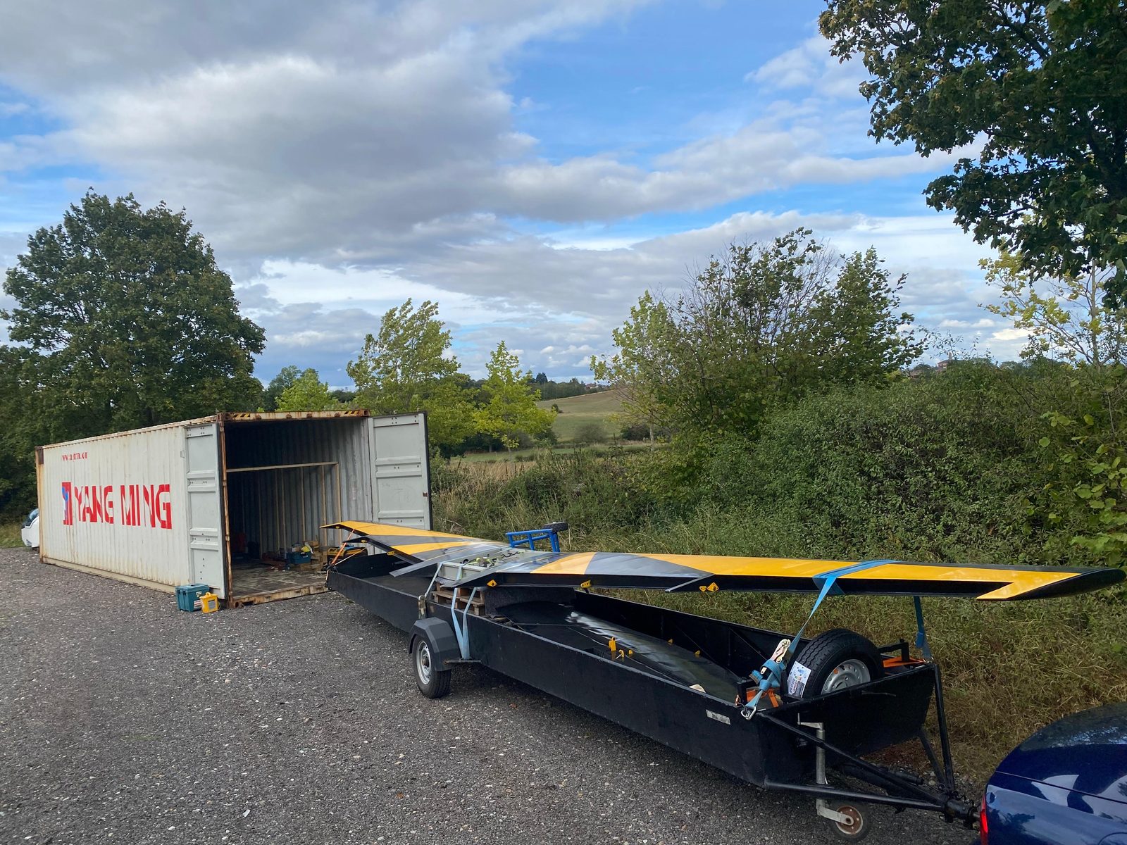Black and yellow wing on a road trailer beside a shipping container