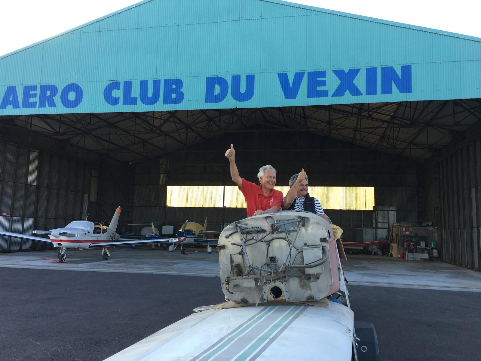 At Aéro-Club du Vexin: two men celebrating over a fuselage tub on a wing